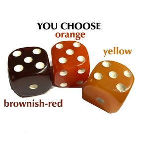 May include: Three dice in shades of brownish-red, orange, and yellow, each with white pips. The text "YOU CHOOSE" and color names are above the dice. The dice are on a white background.