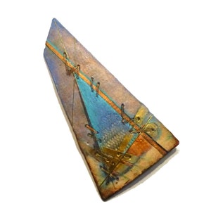 May include: A triangular ceramic wall hanging with a blue, gold, and brown abstract design. The piece is decorated with a series of small, gold metal accents.