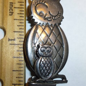 Pu&ograve; includere: Spilla a forma di gufo in tono argento con un gufo pi&ugrave; piccolo sul petto. Il gufo pi&ugrave; grande ha un motivo a rombi sul corpo. La spilla &egrave; alta circa 2,5 cm.