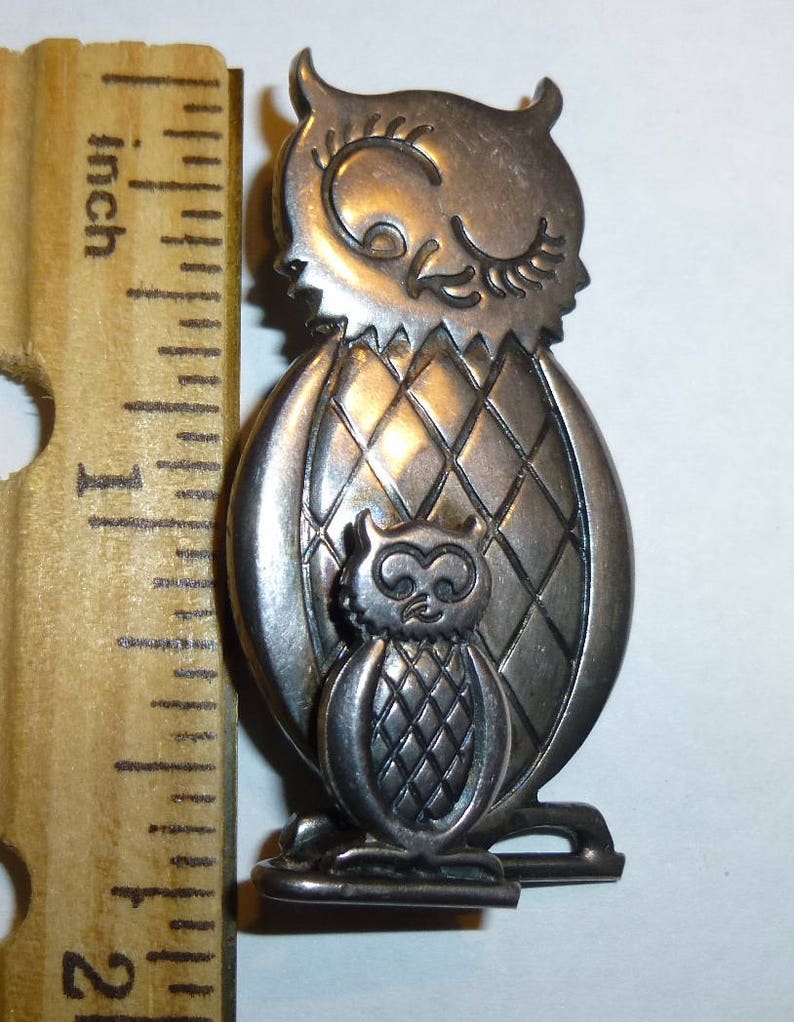 Pu&ograve; includere: Spilla a forma di gufo in tono argento con un gufo pi&ugrave; piccolo sul petto. Il gufo pi&ugrave; grande ha un motivo a rombi sul corpo. La spilla &egrave; alta circa 2,5 cm.