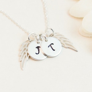 May include: Silver necklace with two small round charms with the letters J and T on them. The charms are attached to a silver angel wing charm.