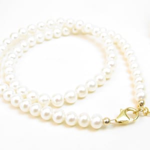 small circle Gold chain link necklace with a cream crystal and oblong gold and pearl charm with lobster claw closure.