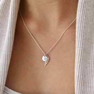 Puede incluir: Un collar de plata con una cadena delicada y un peque&ntilde;o colgante con un ala &uacute;nica y un dije redondo con una letra.