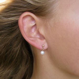 May include: A pair of small gold earrings with a single white pearl dangling from each earring.
