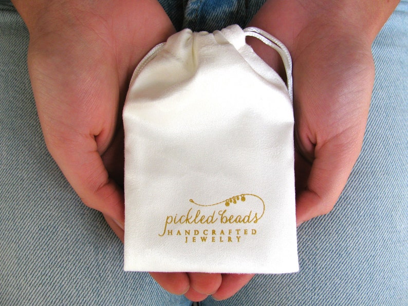 May include: A white drawstring pouch with the text "pickled beads handcrafted jewelry" printed in gold.