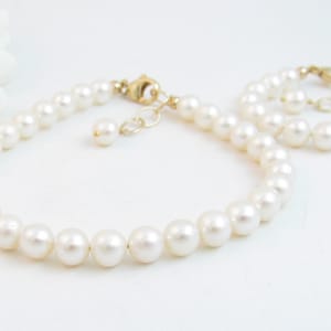 May include: A set of two pearl bracelets with gold clasps. The larger bracelet has a single pearl charm.