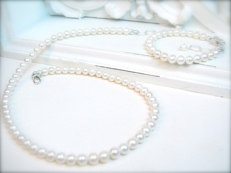 May include: A set of white pearl jewellery, comprising a necklace and a bracelet. Both the necklace and bracelet are made of small, round pearls.
