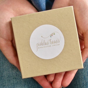 May include: A brown box with a white circle sticker that says "pickled beads handcrafted jewellery" with a colourful string of beads on the sticker.