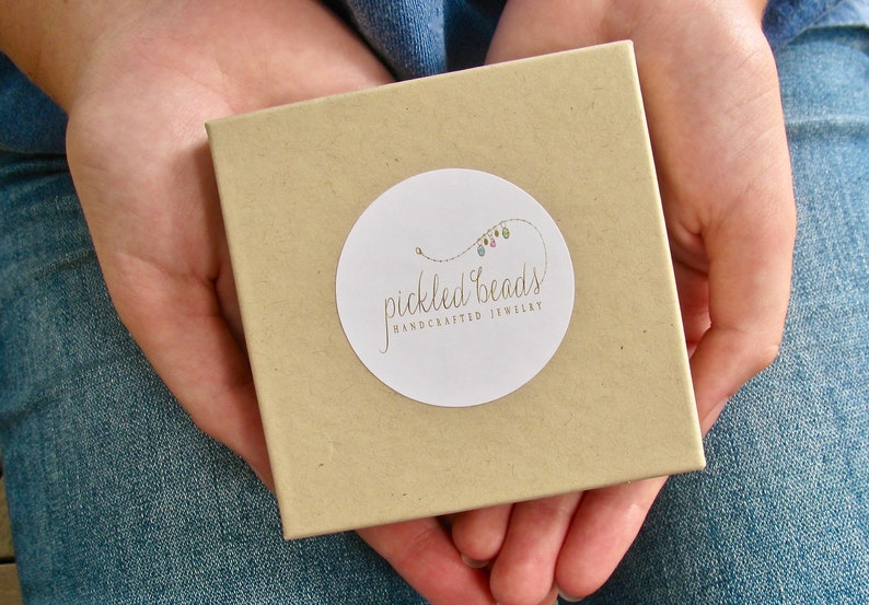 May include: A brown box with a white circle sticker that says "pickled beads handcrafted jewellery" with a colourful string of beads on the sticker.