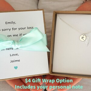 Puede incluir: Una caja de regalo con una cinta azul claro y una nota escrita a mano que dice "Emily, lo siento mucho por tu p&eacute;rdida sobre m&iacute; si estuvieras aqu&iacute;... Con amor, Jaime". La caja contiene un collar de plata con un peque&ntilde;o dije que tiene una letra "K" y un dise&ntilde;o de ala. El texto "4 &euro; Opci&oacute;n de envoltorio de regalo Incluye tu nota personal" est&aacute; impreso en la parte inferior de la caja.