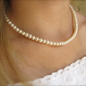 May include: A simple white pearl necklace worn on a person's neck. The necklace is made of small, round pearls.
