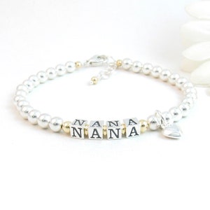Puede incluir: Un brazalete de cuentas plateadas y doradas con un dije de corazón y la palabra "NANA" escrita en cuentas de letras plateadas.