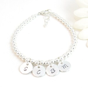 May include: A silver beaded bracelet with four silver charms, each with a letter engraved on it: S, C, B, and M.