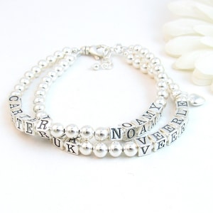 Puede incluir: Dos pulseras de cuentas plateadas con cuentas de letras personalizadas que deletrean los nombres Carter, Rylee, Noah y Amy. Las pulseras están conectadas por un dije de corazón plateado.