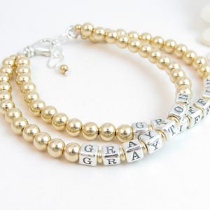 Puede incluir: Pulsera de cuentas doradas y plateadas con los nombres "GRAY" y "TIFFANY" escritos en cuentas plateadas.