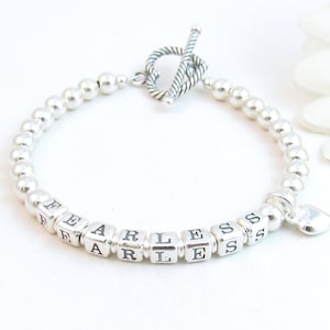 May include: Silver beaded bracelet with a heart charm and the word "FEARLESS" spelled out in silver letter beads.