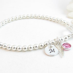 May include: A silver beaded bracelet with a toggle clasp. The bracelet has a charm with the letter "M" and a small pink crystal.