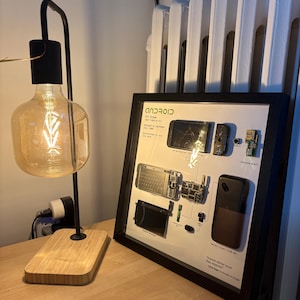 May include: A framed deconstructed HTC Dream smartphone display featuring disassembled components like the logic board, keyboard, and battery cover mounted on a white background with the Android logo and text Always deliver more than expected.