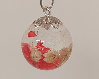 May include: A silver chain necklace with a round, clear glass pendant containing dried red and white flowers. The pendant has a silver filigree design around the top.