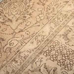 May include: Close-up of a beige and brown vintage rug with intricate floral and geometric patterns. The rug has a distressed look, with faded colors and visible wear, suggesting age and use. The design includes borders and central motifs.