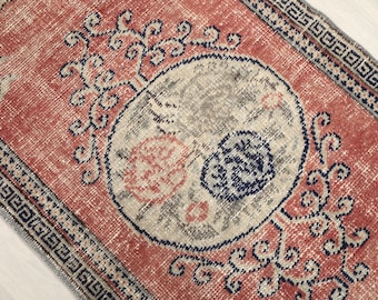 Puede incluir: Una alfombra vintage con fondo rojo y un gran diseño circular de color crema con un patrón floral estilizado. La alfombra tiene un borde azul y blanco con un patrón geométrico.