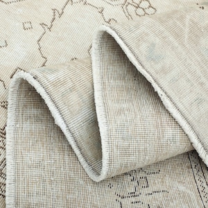 May include: Beige and brown vintage-style rug with a rolled edge, showcasing intricate geometric and floral patterns. The rug's design features a distressed look, adding to its antique aesthetic. The rug is made of a woven material.
