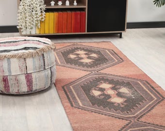 Puede incluir: Una alfombra de pasillo de estilo vintage desgastado en tonos melocotón y gris con patrones geométricos. Un otomán redondo y rayado con flecos está a la izquierda. La alfombra está sobre un suelo de madera clara.