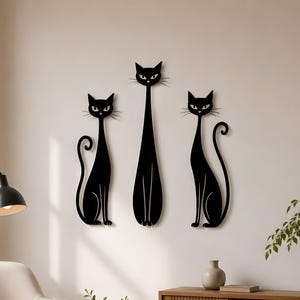 May include: Three black cat wall art silhouettes arranged vertically on a wall. The two outer cats are seated with curled tails, while the central cat is taller and standing. Each cat features pointed ears, almond-shaped eyes, and whiskers.