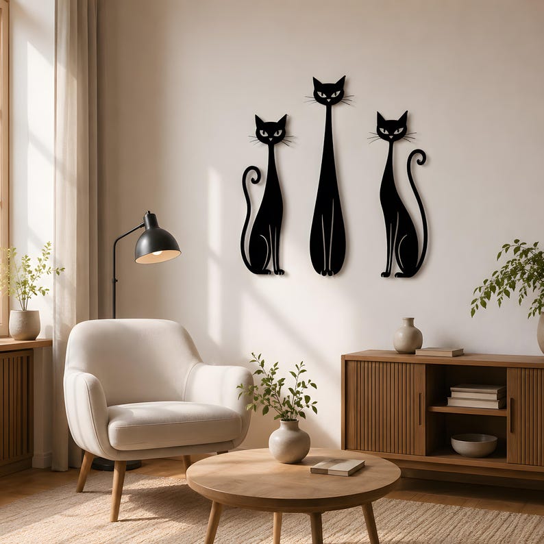 May include: Three black cat wall art silhouettes arranged vertically on a wall. The two outer cats are seated with curled tails, while the central cat is taller and standing. Each cat features pointed ears, almond-shaped eyes, and whiskers.