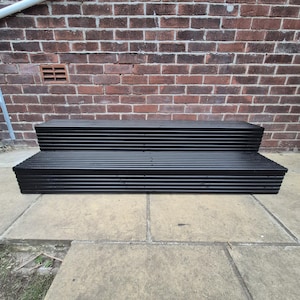 May include: A two-tier black wooden step unit featuring a slatted design on the treads and risers. The structure consists of a wider bottom step and a narrower top step, both constructed with horizontal planks that create a uniform ribbed texture.