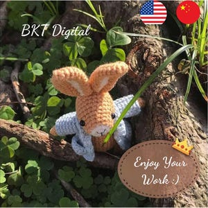 May include: A crocheted bunny rabbit wearing a blue jacket, sitting on a branch with green leaves. The text "Enjoy Your Work :)" is on a brown oval background with a gold crown.