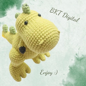 May include: A crocheted yellow dinosaur toy with black eyes and a green leafy tail. The toy is on a white background with green watercolor splatter. The text "BKT Digital" and "Enjoy :)" is also on the background.