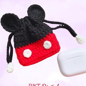 Könnte beinhalten: Eine rote und schwarze gehäkelte Airpod-Hülle in Form von Mickey Mouse. Die Hülle hat weiße Knöpfe und einen Kordelverschluss. Die Hülle liegt neben einer weißen Airpod-Hülle.
