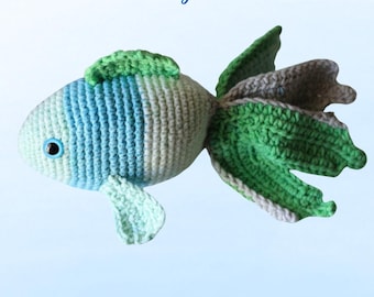 Puede incluir: Un juguete de pescado de crochet verde, azul y gris con el texto "Lovely Fish" arriba y "BKT Digital" abajo.