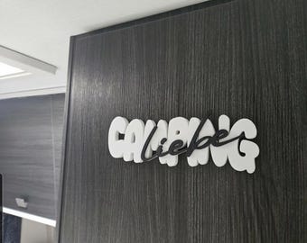 May include: A white and black wooden sign that says "CAVABANG liebe" in a stylized font. The sign is mounted on a dark gray wooden surface with vertical grain.