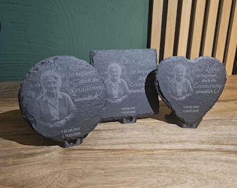 May include: Three dark gray slate memorial plaques in circle, square, and heart shapes. Each features an engraved portrait of an elderly person, the German text Das Leben ist begrenzt doch die Erinnerung unendlich, and the dates 07.09.1941 and 18.05.2026.
