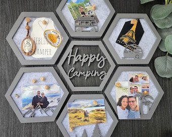 May include: A set of six grey hexagonal wall-mounted display frames with light grey felt backings. The frames feature wooden push pins, various travel photographs, a metal Eiffel Tower cutout, a religious pendant, and a central frame with the text Happy Camping.