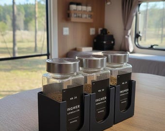 May include: Three square glass spice jars with silver metal lids, each held in a black matte plastic holder. The jars feature black labels with white text reading NR. 28 INGWER GEMAHLEN VUMSEL, NR. 20 INGWER GEMAHLEN, and NR. 20 INGWER GEMAHLEN.