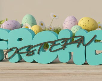 May include: A teal-colored wooden sign that reads "Frohe Ostern" in German, with a dark brown cursive overlay. Pastel-colored speckled Easter eggs and daisies are in the background, with green grass and leaves. The sign is on a wooden surface.