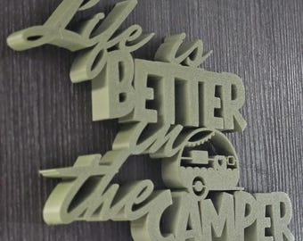 May include: A sage green 3D-printed sign with the phrase "Life is BETTER in the CAMPER." The word "BETTER" is in bold, capital letters. A small camper graphic is integrated into the design, adding a touch of adventure.