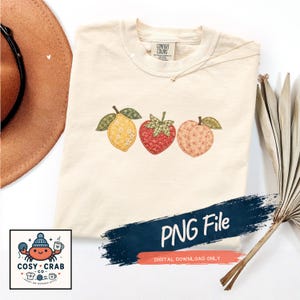 May include: A cream-colored t-shirt featuring an embroidered-style graphic of a yellow lemon, a red strawberry, and a peach, each with green leaves. The shirt has a Comfort Colors label at the neck and includes a PNG File digital download notice.
