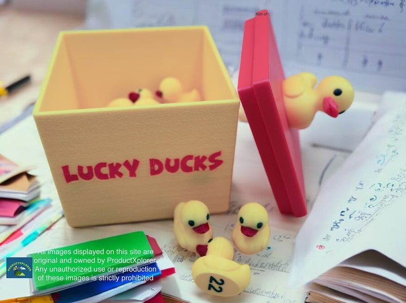 May include: A yellow box with the words "LUCKY DUCKS" printed on the front. The box is open and filled with yellow rubber duck toys. The box is sitting on a table with a stack of papers.