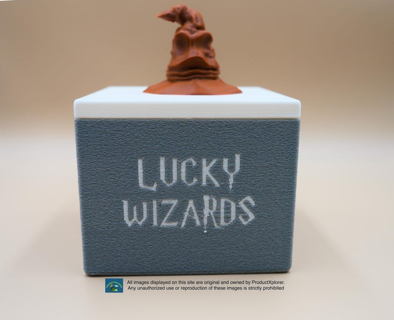 Pu&ograve; includere: Una scatola grigia con le parole "LUCKY WIZARDS" stampate in bianco. Un Cappello Parlante marrone della serie Harry Potter si trova sopra la scatola.