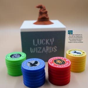 Pu&ograve; includere: Un set di gettoni da gioco colorati con diversi stemmi di casa e le parole "Saggezza" e "Coraggio" stampate su di essi. I gettoni sono impilati davanti a una scatola bianca con le parole "Lucky Wizards" stampate su di essa. Un Cappello Smistatore marrone si trova sopra la scatola.