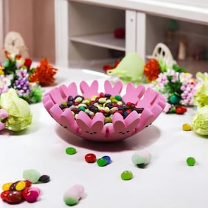 May include: A pink bunny-shaped bowl filled with colorful candy. The bowl is made of ceramic and has a glossy finish. The candy is a mix of different colors and shapes.