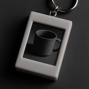 Peut inclure: Un porte-cl&eacute;s rectangulaire blanc avec un anneau argent&eacute;. Le porte-cl&eacute;s pr&eacute;sente une tasse grise &agrave; l'int&eacute;rieur d'un cadre gris. La tasse a une anse et est centr&eacute;e dans le cadre. Le fond est gris fonc&eacute;.