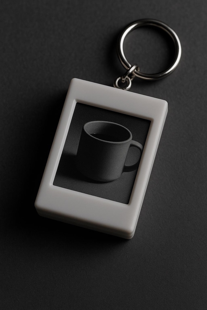 Peut inclure: Un porte-cl&eacute;s rectangulaire blanc avec un anneau argent&eacute;. Le porte-cl&eacute;s pr&eacute;sente une tasse grise &agrave; l'int&eacute;rieur d'un cadre gris. La tasse a une anse et est centr&eacute;e dans le cadre. Le fond est gris fonc&eacute;.