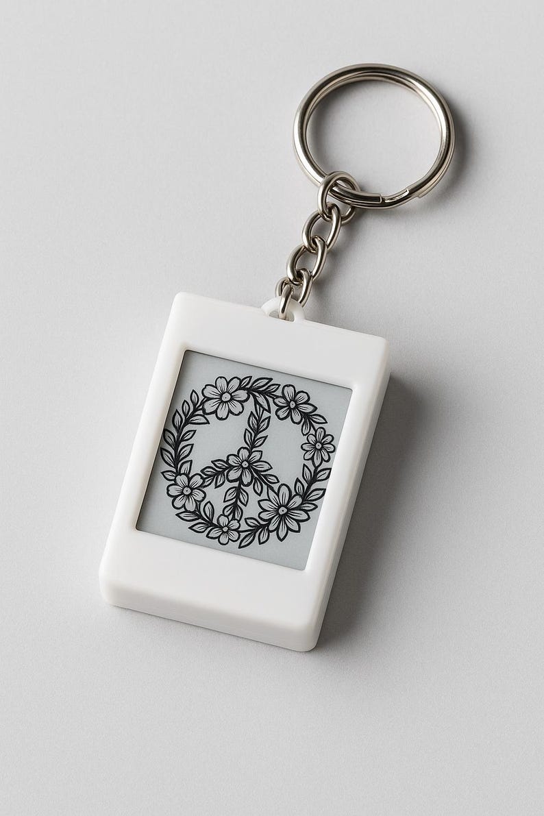 Peut inclure: Porte-cl&eacute;s rectangulaire blanc avec une cha&icirc;ne et un anneau argent&eacute;s. Le porte-cl&eacute;s pr&eacute;sente un insert gris avec un motif de signe de paix floral noir. Le signe de paix est entour&eacute; d'une couronne de fleurs et de feuilles.