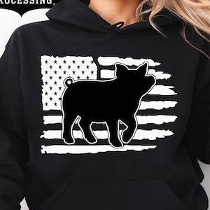 Può includere: Felpa con cappuccio nera con un design a bandiera americana bianca e una silhouette di maiale nera. La felpa con cappuccio ha una tasca frontale e un cappuccio con coulisse. Le parole "FAST PROCESSING" sono in uno striscione nero in alto a sinistra.