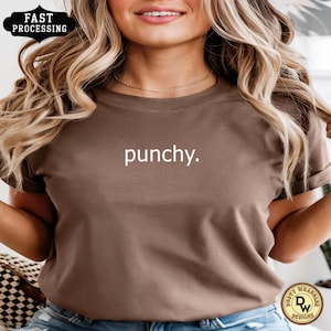 May include: A brown t-shirt with the word "punchy" printed in white. The shirt has short sleeves and a crew neck. The image also includes a "Fast Processing" badge and a logo.